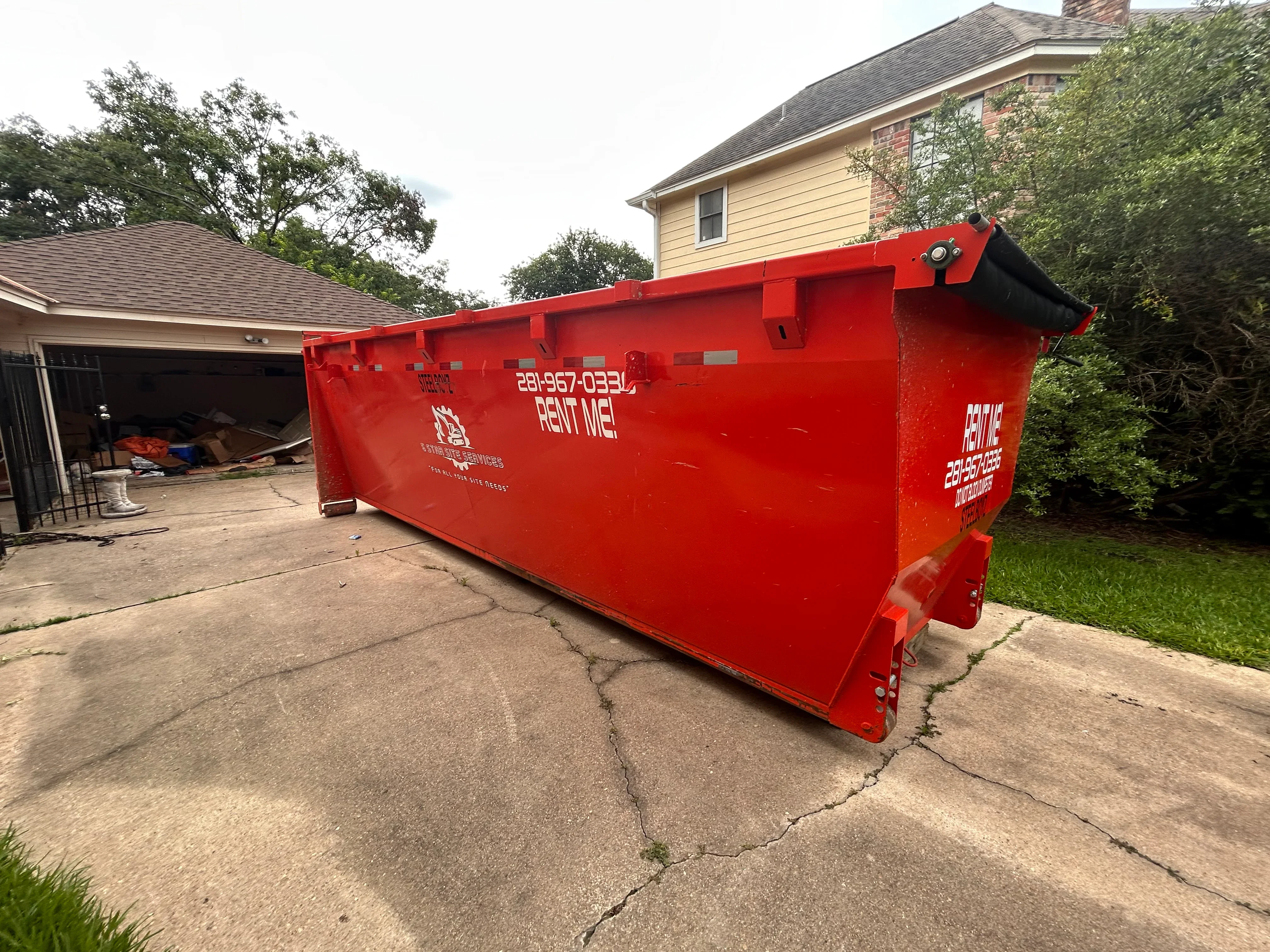 Red roll-off dumpster container on residential driveway for debris removal and hauling