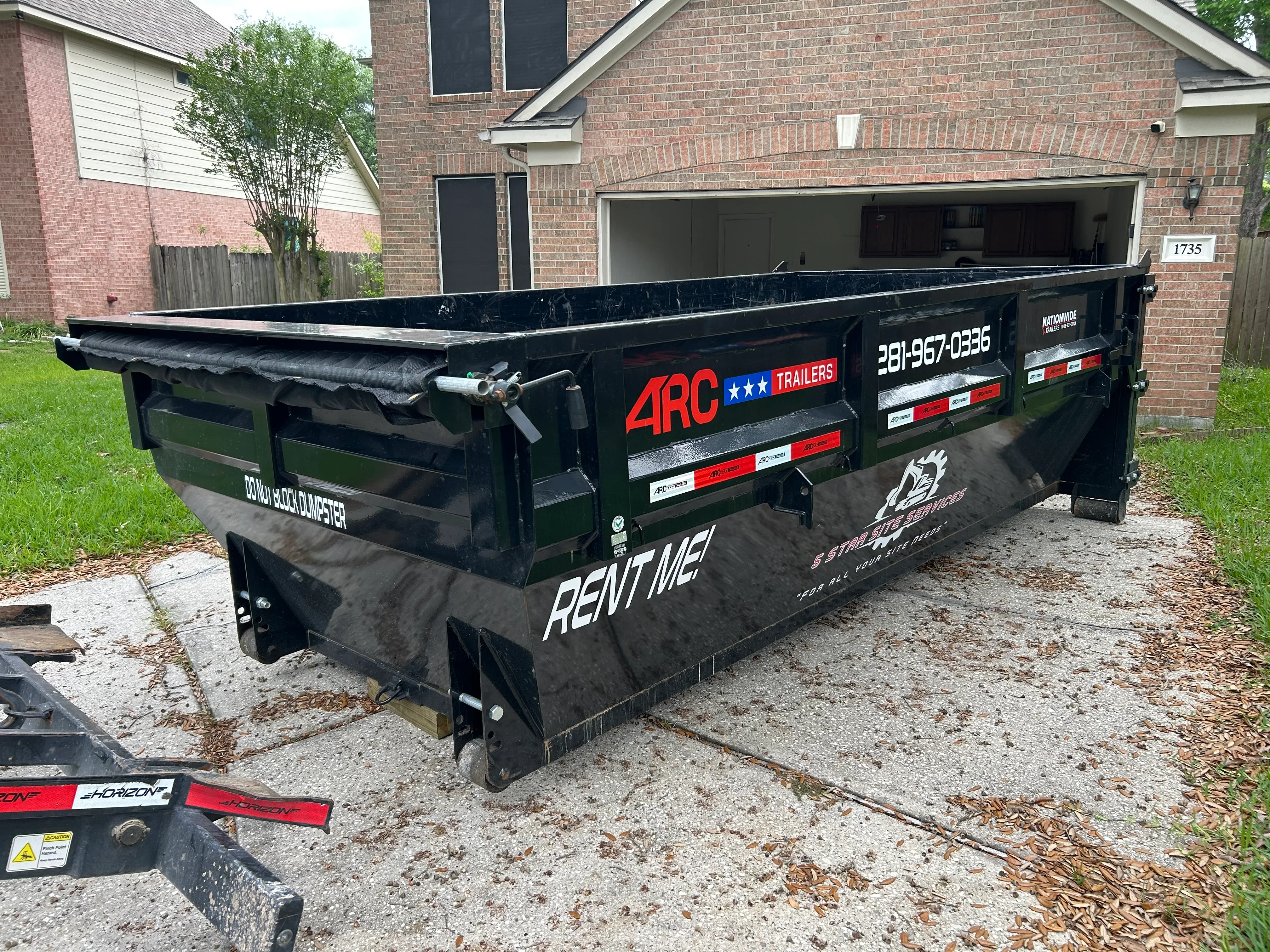 Black steel dumpster trailer with red safety stripes positioned in residential driveway