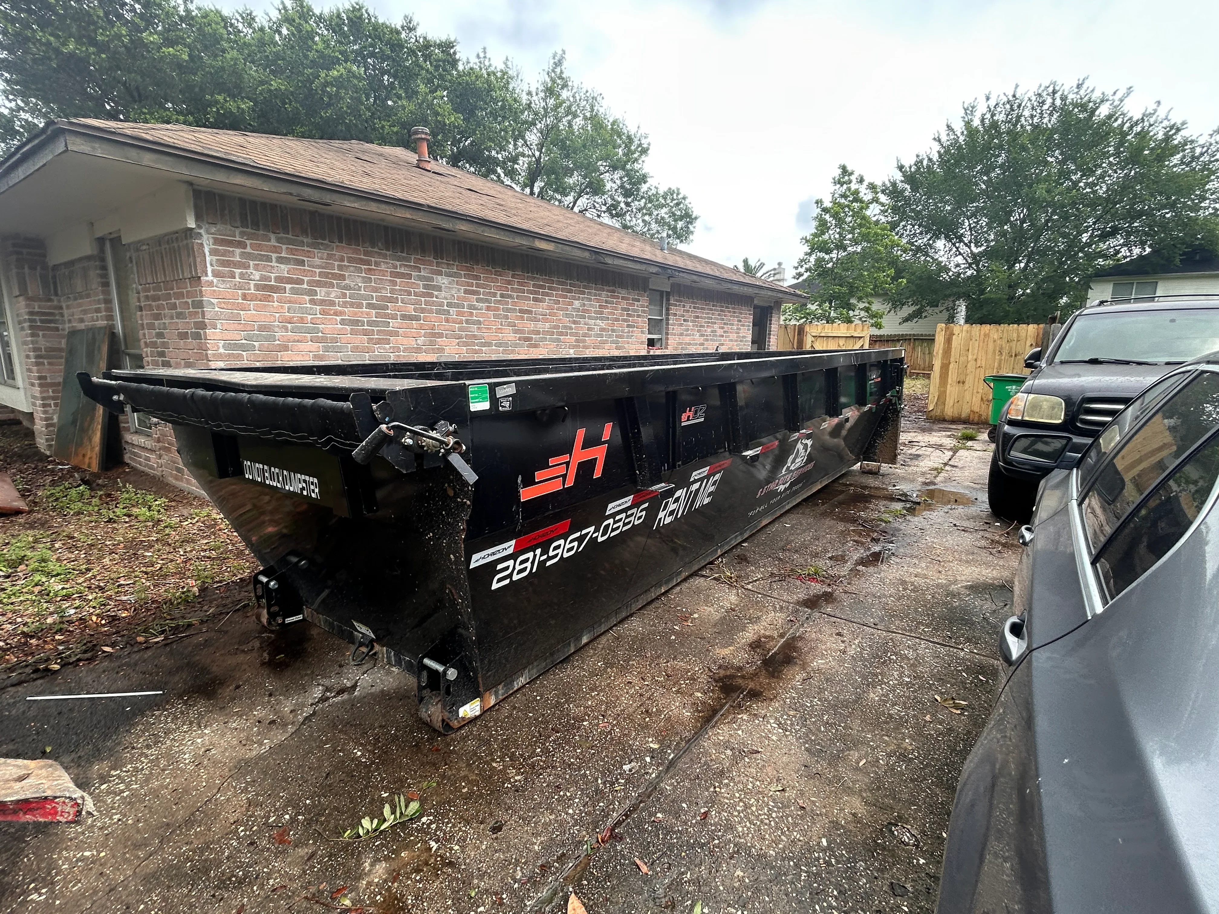 Black roll-off dumpster at brick residential home with hydraulic lift system