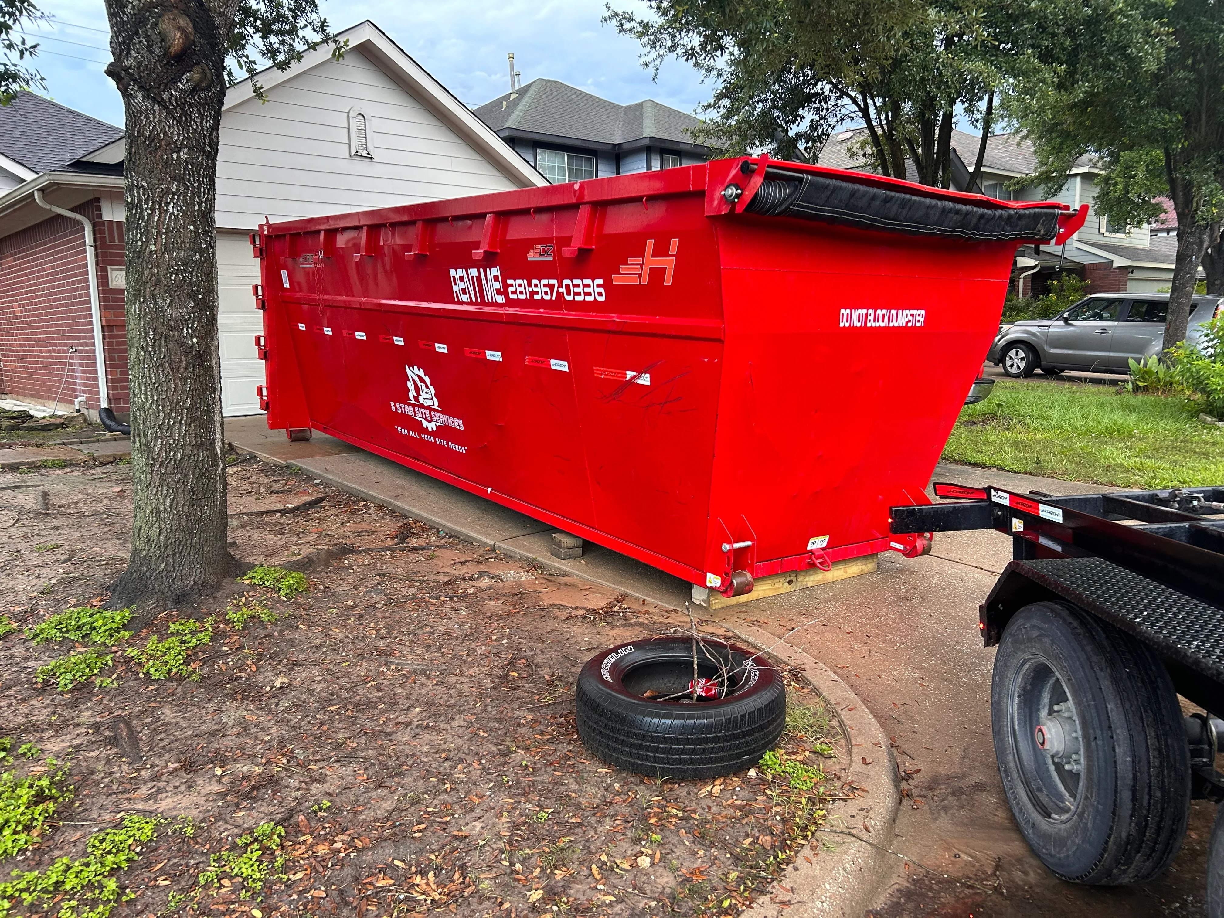Red roll-off dumpster container positioned in residential driveway for debris hauling