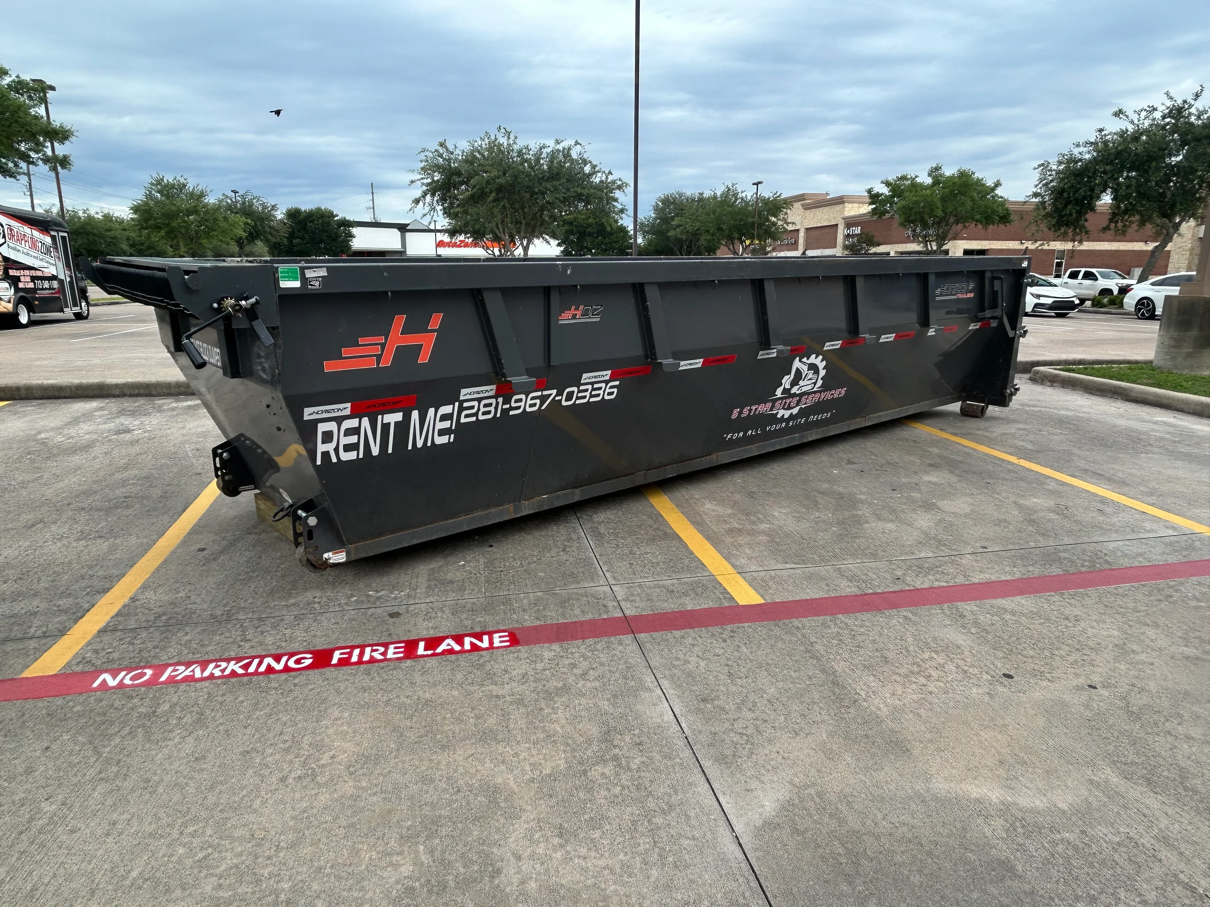 Black steel roll-off dumpster with orange branding in commercial lot