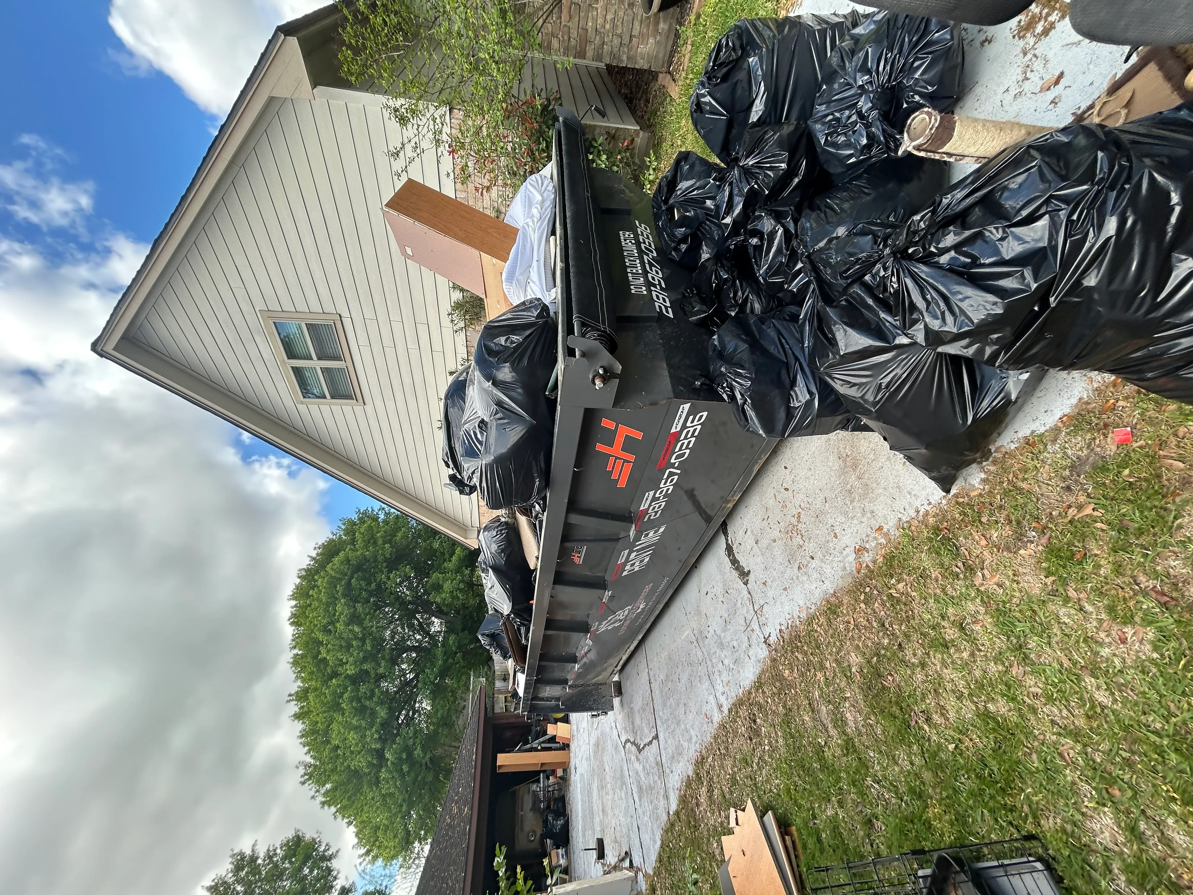 Dumpster filled with black bags of demolition debris and wood materials from residential project