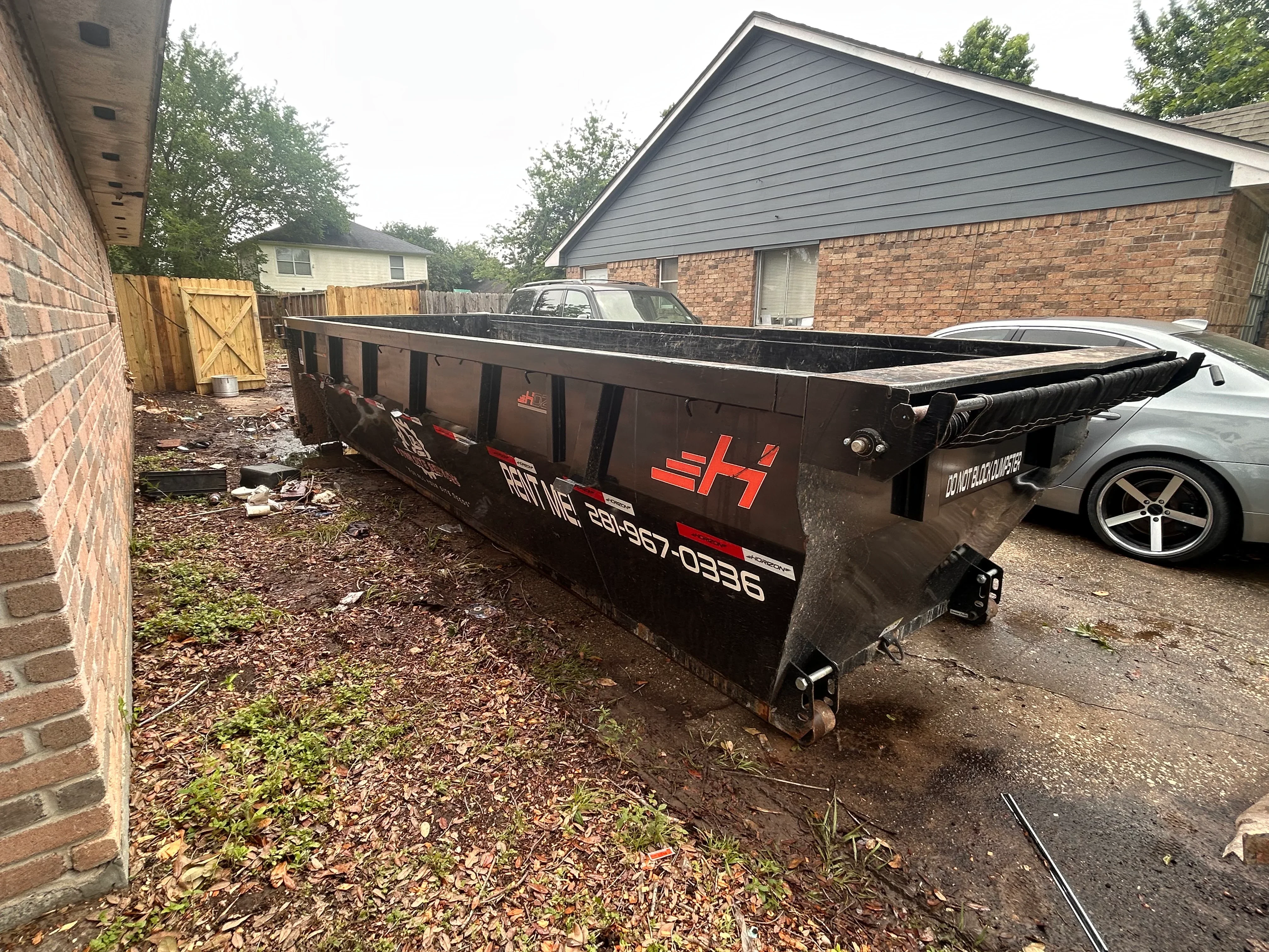 Black roll-off dumpster with hydraulic lift system in residential driveway
