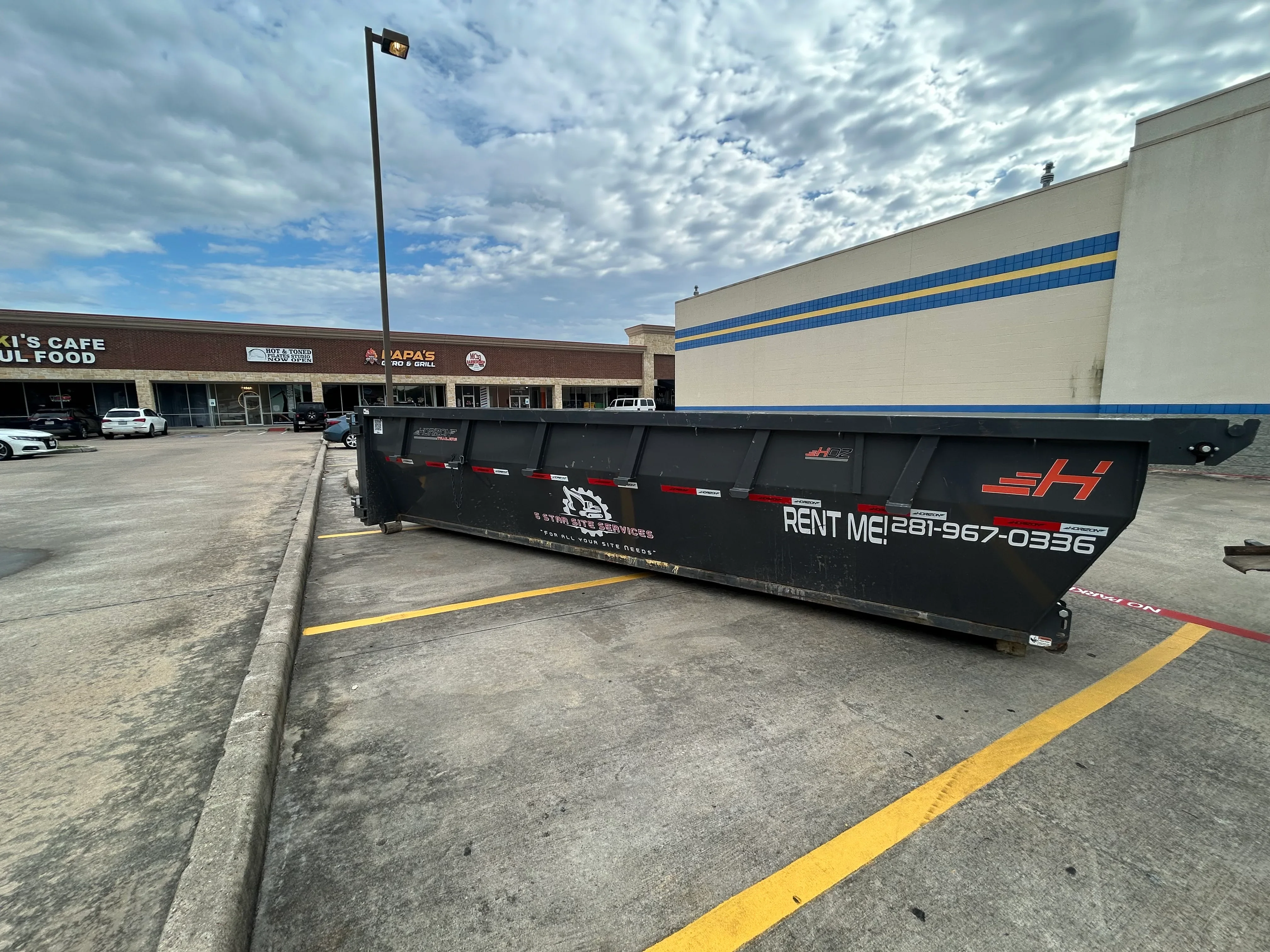 Black roll-off dumpster with red reflective striping in commercial parking lot