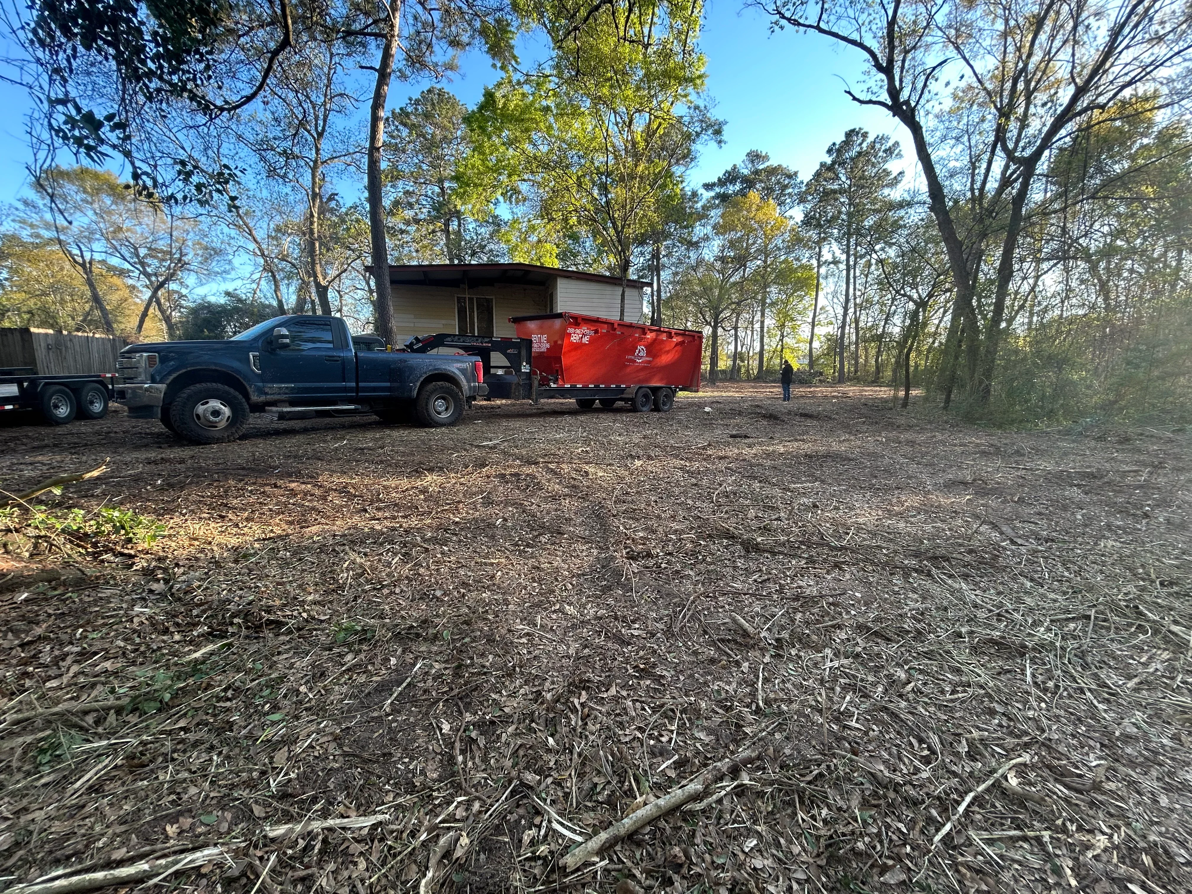 Cleared wooded lot with debris removal equipment and red hauling trailer staged on-site