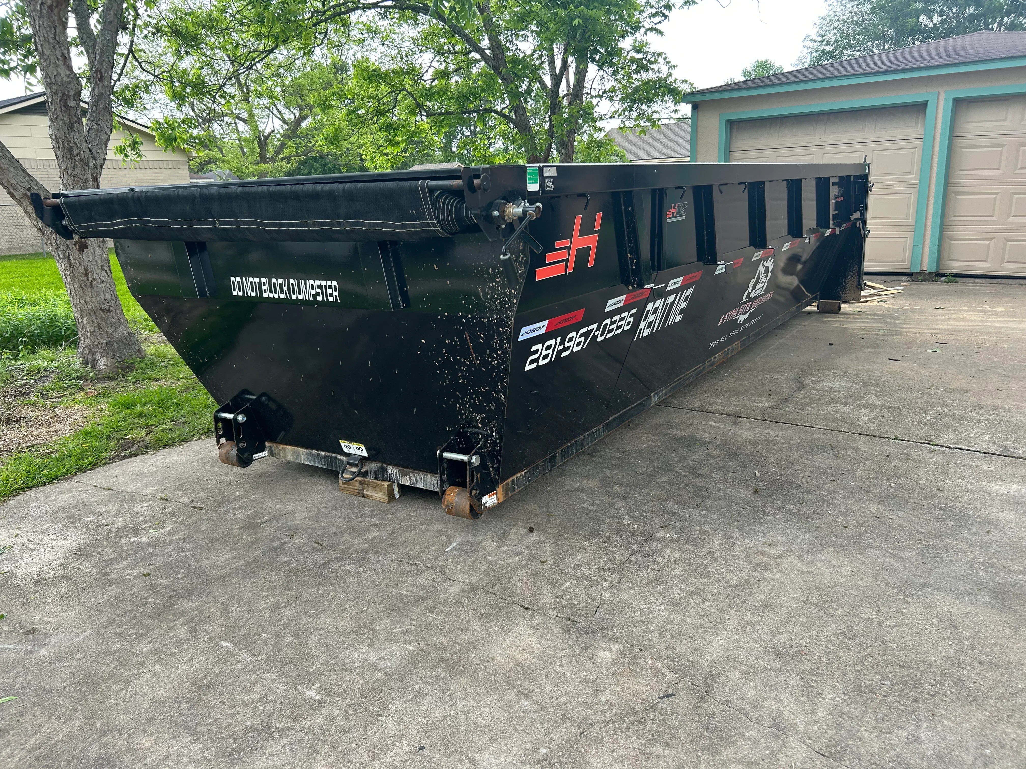 Black roll-off dumpster with hydraulic lift system positioned on residential driveway