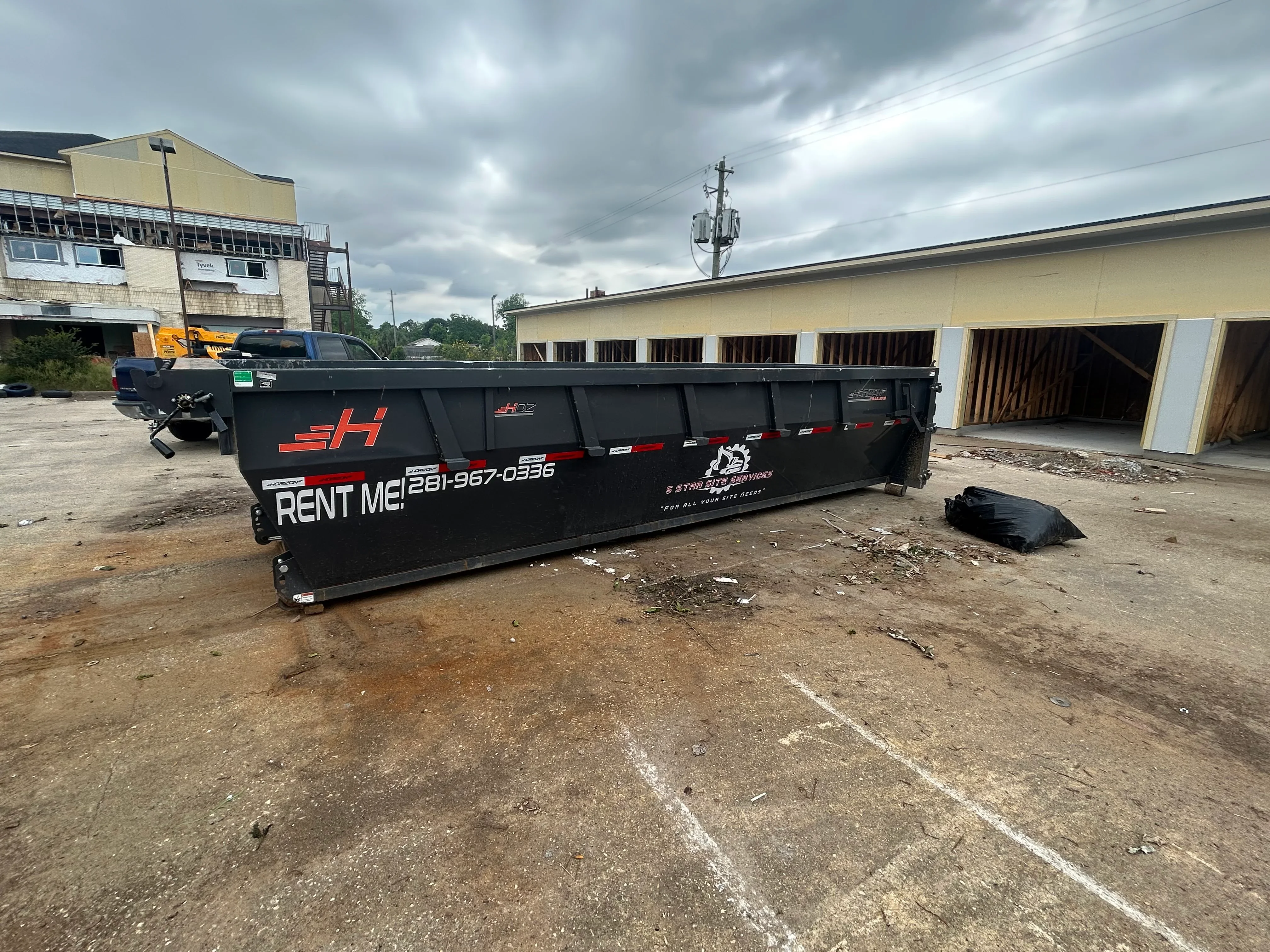 Black steel roll-off dumpster container with reflective striping on dirt lot